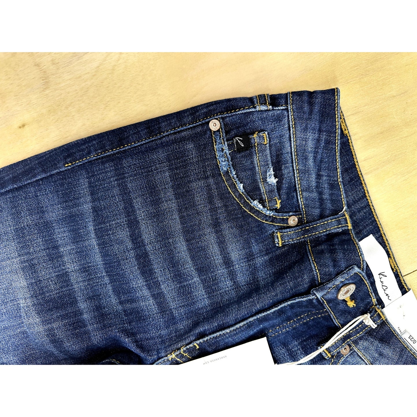 Close-up of blue jeans with a visible brand label on a beige background