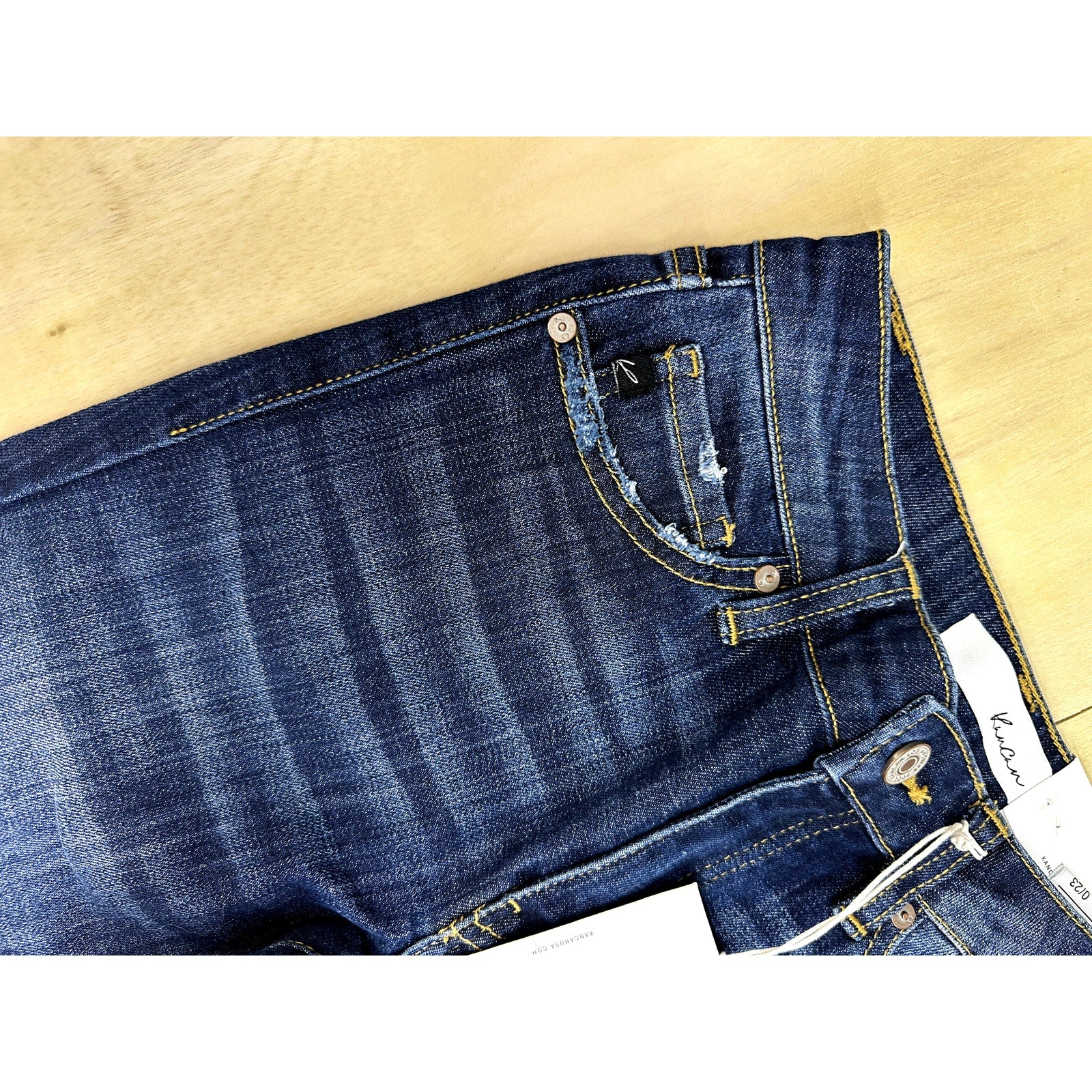 Close-up of blue jeans with a visible brand label on a beige background