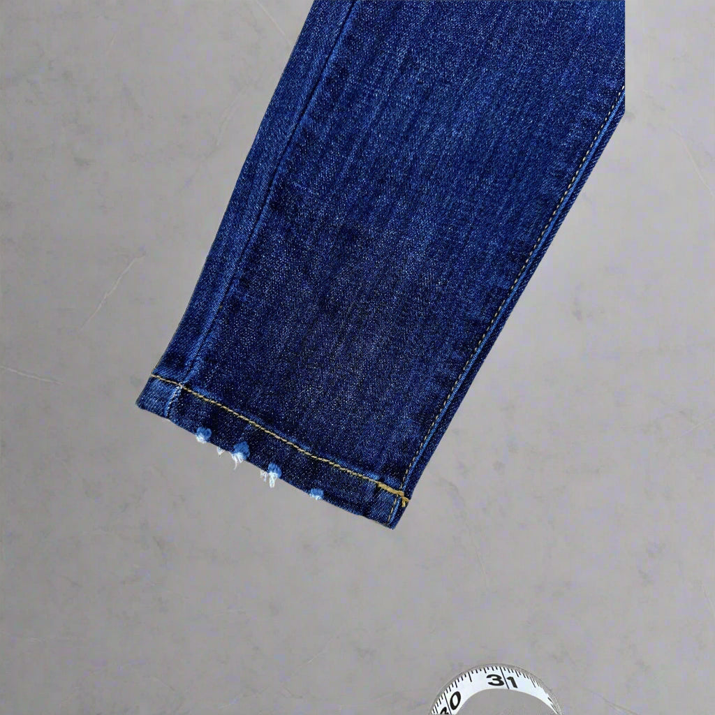 Close-up of blue jeans hem with a measuring tape on a wooden surface